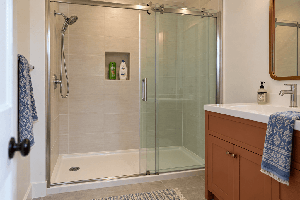Sliding glass shower door open on the left, with overlapping panels beside a terracotta vanity on the right.