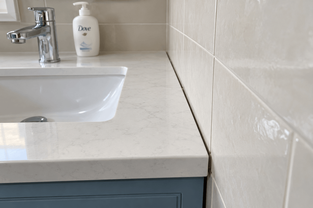 Narrow unsealed joint between a white bathroom vanity countertop and the adjacent cream tiled wall.